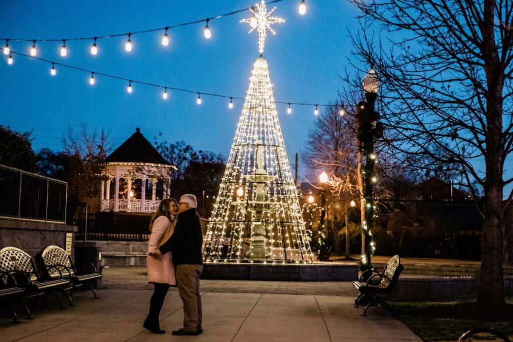 A couple embraces under holiday lights during their Christmas vacation in Madison, GA